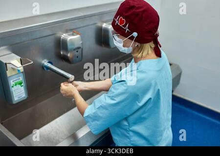 Ein medizinischer Mitarbeiter befolgt die richtigen Handwaschtechniken an einem Spital, um Hygiene zu gewährleisten und Infektionen zu verhindern. Uniform und Protektiv tragen Stockfoto