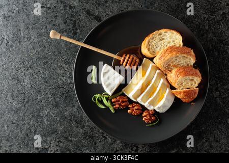 Camembert-Käse mit Honig, Croissants und Walnüssen auf einem schwarzen Teller. Draufsicht. Stockfoto