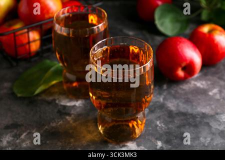 Gläser mit frischem Apfelwein und Früchten auf dunklem Hintergrund, Nahaufnahme Stockfoto