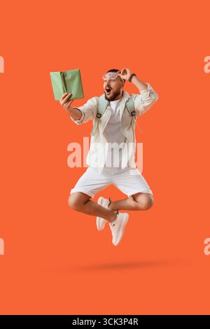 Überraschter junger Mann mit Buchsprung auf orangem Hintergrund Stockfoto