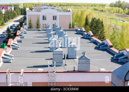 Serie von metallischen Lüftungsstapeln, die auf einem flachen Dach für die Umluft und Abluft in Innenräumen installiert sind, mit selektivem Fokus auf den Lüftungsschacht Stockfoto