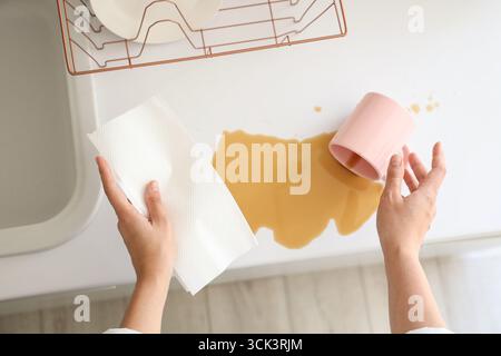 Weibliche Hände mit Papierhandtuch wischen verschütteten Kaffee auf der Theke in der Küche ab, Blick von oben Stockfoto