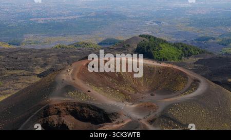 Blick aus der Vogelperspektive auf den vulkanischen Krater des Ätna mit leuchtenden roten und schwarzen Lavasteinen. Blick auf schwarze vulkanische Asche, rote Hänge und grüne Vegetation. Stockfoto