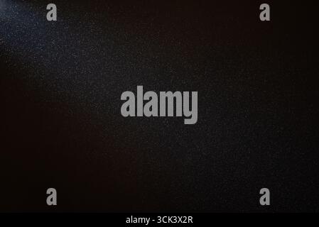 Lichtstrahl beleuchtet unzählige Staubpartikel, die in der Luft vor einem schwarzen Hintergrund schweben, und erzeugt einen faszinierenden und ätherischen Effekt Stockfoto