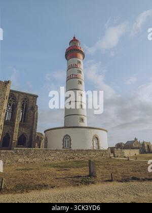 Blick auf den majestätischen Leuchtturm Saint-Mathieu mit seinen roten und weißen Streifen vor dem Hintergrund der alten Steinruinen Plougonvelin, Bretagne, Frankreich. Stockfoto