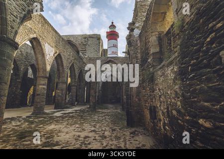 Der Blick auf einen rot-weißen Leuchtturm erhebt sich über den überdachlosen Ruinen der Abtei Saint-Mathieu, ein Ort, an dem die Geschichte aus Steinmauern flüstert, Plougonvelin, Stockfoto