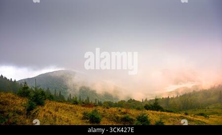 Berge im Freien mit bewölktem Morgen im Herbst. Nebeliger Natur Hintergrund im Hochland der ukraine. Dramatisches Wetter Stockfoto