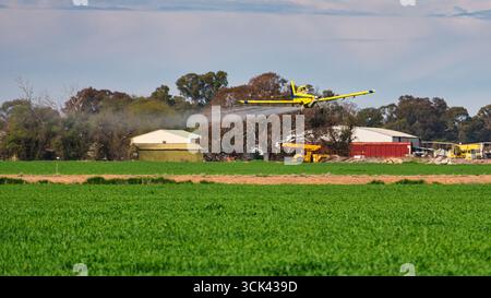 Yarrawonga, Victoria, Australien - 25. August 2025: Lufttraktor sprüht große Mengen von Feldfrüchten auf Yarrawonga Ackerland in der Nähe von Bäumen und Schuppen Stockfoto