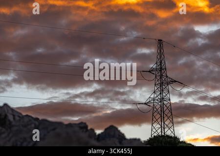 Hochspannungsmasten gegen den Himmel während Sonnenuntergang, Stromleitung, Sonnenuntergang mit bewölktem orangefarbenen Himmel Stockfoto