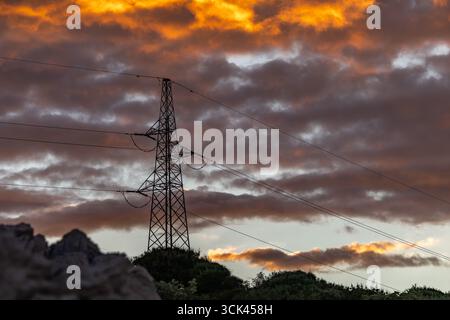 Hochspannungsmasten gegen den Himmel während Sonnenuntergang, Stromleitung, Sonnenuntergang mit bewölktem orangefarbenen Himmel Stockfoto