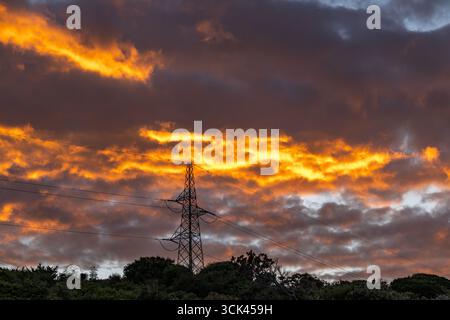 Hochspannungsmasten gegen den Himmel während Sonnenuntergang, Stromleitung, Sonnenuntergang mit bewölktem orangefarbenen Himmel Stockfoto