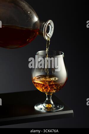 Cognac oder Brandy wird in ein Glas gegossen. Brandy-Scharfschütze auf dunklem Hintergrund. Stockfoto