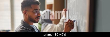 Kopfzeile von Young Adult biracial man, der auf Blackboard in Sprachunterricht schreibt Stockfoto