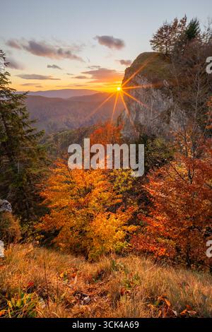 Blick auf die strahlende Sonne über zerklüfteten Klippen und herbstbemalten Bäumen, eine Symphonie der Farben in der goldenen Stunde, Majerova Skala Felsen, Staré Hory, Banskobystrický kraj, Slowakei. Stockfoto