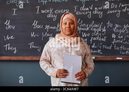 Junge Erwachsene muslimische Frau, die ein Notizbuch hält, steht in der Sprachschule Stockfoto