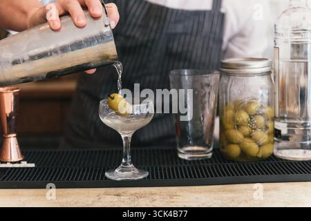 Der Barkeeper gießt Martini aus dem Shaker ins Glas Stockfoto