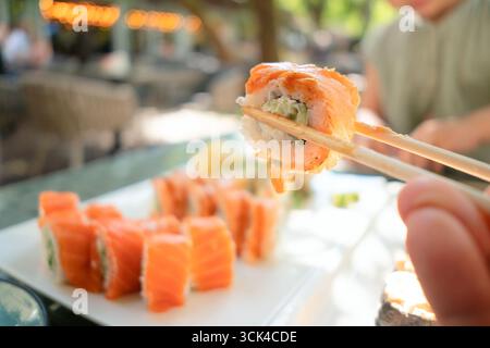 Authentisches japanisches Sushi-Brötchen mit Premium-Lachs und Gurke, fachmännisch mit Essstäbchen in einem traditionellen Restaurant gehalten. Stockfoto