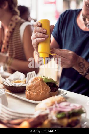 Zugeschnittene Aufnahme von Paaren, die Mayonnaise auf Burger im Straßencafé stecken. Das Bild wurde am 11.01/17 um 12:24 Uhr heruntergeladen Stockfoto