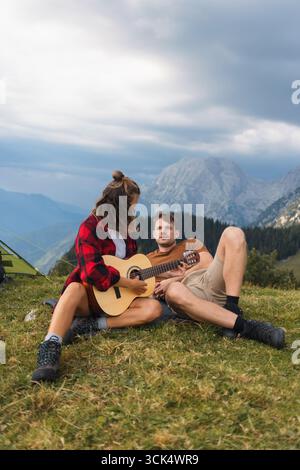 Junge Paare campen in den Bergen, spielen Gitarre, genießen Freiheit und verbinden sich mit der atemberaubenden Natur. Stockfoto
