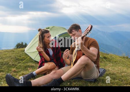 Junge Paare campen in den Bergen, spielen Gitarre, genießen Freiheit und verbinden sich mit der atemberaubenden Natur. Stockfoto