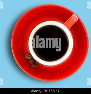 Ein Blick von oben auf eine rote Kaffeetasse gefüllt mit schwarzem Kaffee auf einer passenden Untertasse, begleitet von ein paar Kaffeebohnen. Stockfoto