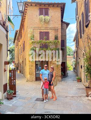 Touristen, die Sommerferien in der Altstadt von Siena genießen. Lächelnde Eltern und Kind stehen vor rustikaler italienischer Architektur mit Balkonblumen Stockfoto