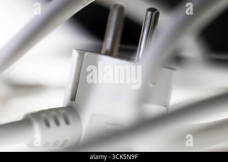 Weißer Netzstecker, Schuko-Stecker mit verwickeltem Netzkabel, Anordnung vor schwarzem Hintergrund und mit Unschärfe, Fokus auf Kontaktstifte, symbolisches Bild Stockfoto