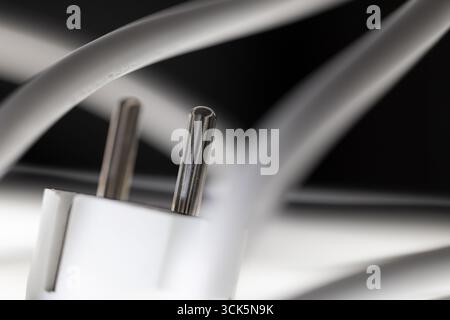 Weißer Netzstecker, Schuko-Stecker mit verwickeltem Netzkabel, Anordnung vor schwarzem Hintergrund und mit Unschärfe, Fokus auf Kontaktstifte, symbolisches Bild Stockfoto