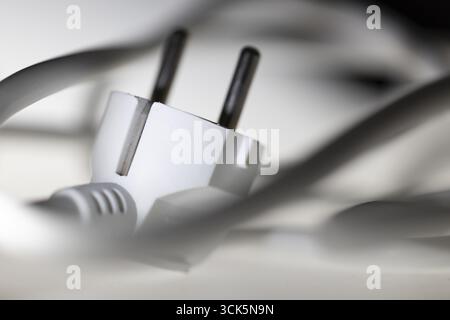 Weißer Netzstecker, Schuko-Stecker mit verwickeltem Netzkabel, Anordnung vor schwarzem Hintergrund und mit Unschärfe, symbolisches Bild für Stromverbrauch A Stockfoto