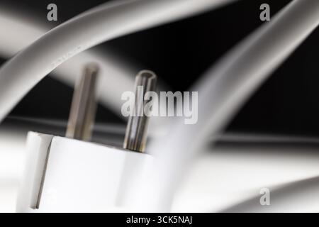 Weißer Netzstecker, Schuko-Stecker mit verwickeltem Netzkabel, Anordnung vor schwarzem Hintergrund und mit Unschärfe, Fokus auf Kontaktstifte, symbolisches Bild Stockfoto