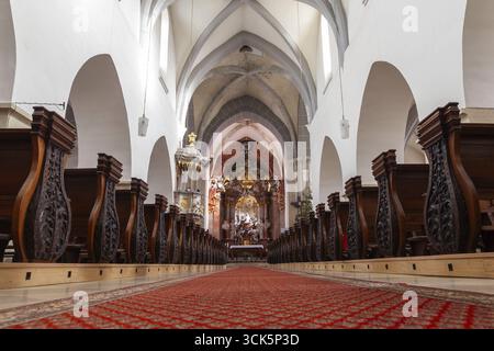 Längliches Kircheninnere mit kunstvoll geschnitzten Bänken und rotem Teppich Laa an der Thaya Pfarrkirche Weinviertel Niederösterreich Österreich Stockfoto