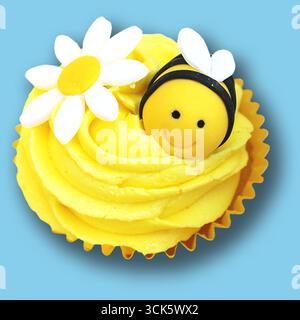 Ein fröhlicher gelber Cupcake mit einer lächelnden Biene und weißen Blumen, perfekt für Feiern oder süße Leckereien. Stockfoto