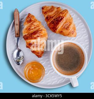Eine gemütliche Frühstücksszene mit zwei Croissants, einer Tasse Kaffee und einem Glas Marmelade auf einem weißen Teller. Stockfoto