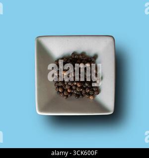 Eine Nahaufnahme der schwarzen Pfefferkörner, die sich in einer kleinen weißen Schale stapeln und deren Textur und Farbe hervorheben. Stockfoto
