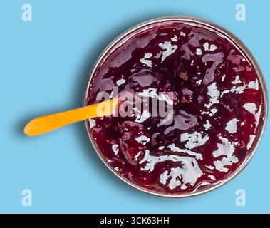 Aus nächster Nähe ein Glas mit dunkler Fruchtmarmelade mit einem Holzlöffel, das seine glänzende Textur und satte Farbe zeigt. Stockfoto