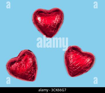 Drei leuchtend rote Pralinen in Herzform, die zusammen angeordnet sind und Liebe und Zuneigung symbolisieren. Stockfoto