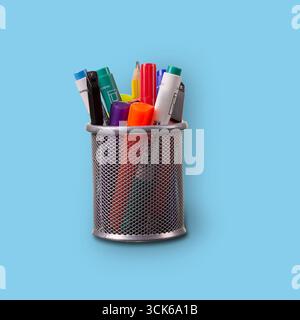 Ein Stifthalter aus Metall, gefüllt mit verschiedenen farbigen Markierungen und Stiften, ideal für die Organisation von Schreibgeräten auf einem Schreibtisch. Stockfoto