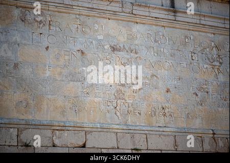Nahaufnahme einer verwitterten lateinischen Inschrift auf der antiken römischen Trophäe der Alpen in La Turbie, Provence, Frankreich, mit geschnitzten Steindetails. Stockfoto