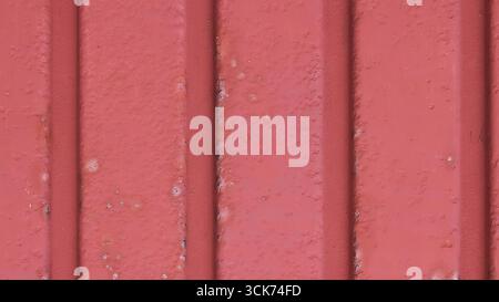 Dieses Bild zeigt eine strukturierte rote Wand mit vertikalen Linien, die ein schlichtes, aber auffälliges Design zeigt. Stockfoto