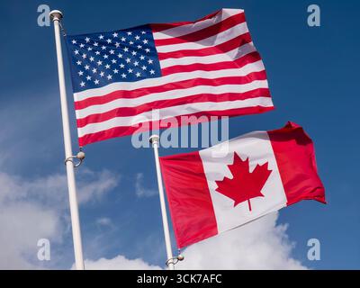 Amerikanische Flagge mit kanadischer Flagge im Wind, Wolken und blauem Himmel dahinter. Die Stars and Stripes und die Maple Leaf Flags USA/KANADA Stockfoto