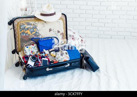Offener Koffer der Frau auf einem Bett mit Kleidung und Accessoires Stockfoto