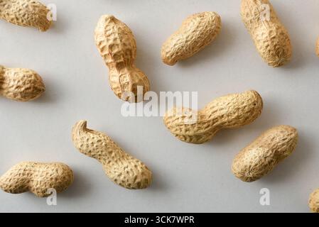 Detail mehrerer Erdnüsse in der Schale, die ihre Form und Textur auf einem weißen Tisch zeigen. Draufsicht. Stockfoto