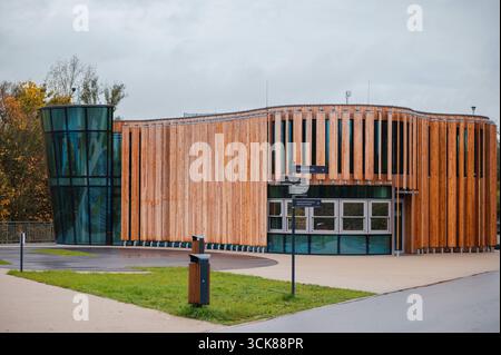 Modernes architektonisches Gebäude mit Holzfassade und Glaselementen, umgeben von Grün und Wegen Stockfoto