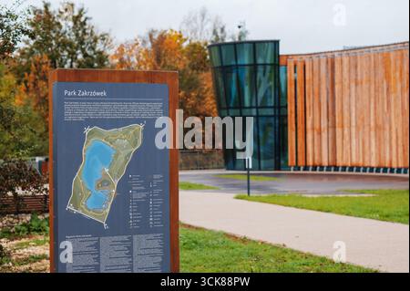 Informationstafel im Park Zakrzówek mit modernem Gebäude und Herbstbäumen. Stockfoto