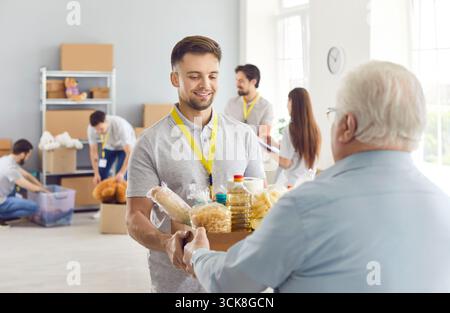 Ein Freiwilliger von einer Wohltätigkeitsorganisation gibt einem armen älteren Mann eine Nahrungsmittelhilfe Stockfoto