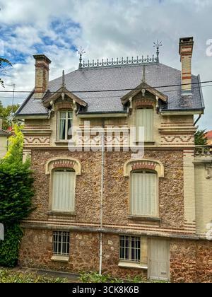 Charmantes historisches französisch mit Stein- und Ziegelfassade, Schieferdach, Schornsteinen und traditionellen Fensterläden umgeben von Grün Stockfoto