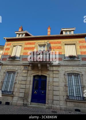 Malerische Hous in chalons en Champagne, mit beigefarbenen Steinen und roten Ziegelsteinen, schmiedeeisernem Balkon mit Blumen und einer auffälligen blauen Doppeltür Stockfoto
