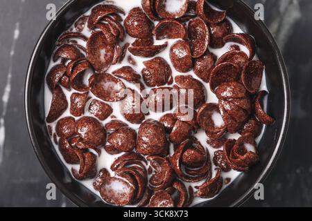 Schüssel mit Schokoladenmüsli und Milch. Zum Frühstück gab es knusprige süße Flocken. Morgenmahlzeit mit Milchernährung. Stockfoto