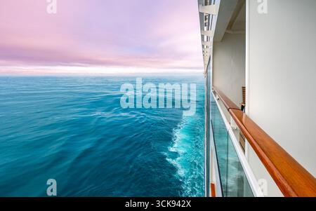 Farbenfrohes Reisefoto eines Kreuzfahrtschiffs, das auf dem Meer segelt, mit Blick auf den Horizont und einen rosafarbenen Sonnenuntergang. Stockfoto