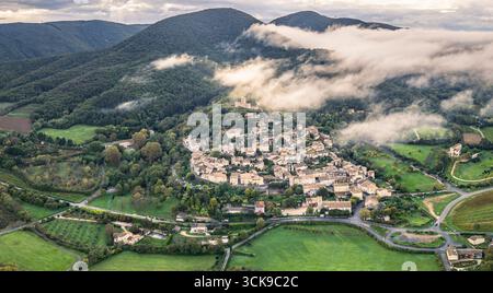 Blick aus der Vogelperspektive auf das Dorf Mirmande in Frankreich mit Morgennebel über den Hügeln – malerische mittelalterliche Stadt umgeben von üppig grünen Wäldern und Landschaft Stockfoto